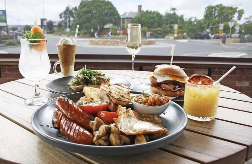 A cooked breakfast with sausages, eggs, mushrooms, beans and a breakfast burger, with drinks